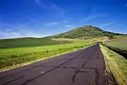 Small paved road approaching a hill surrounded by fields