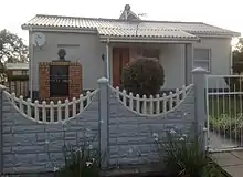 A small, detached one-story house. The walls are a pale colour, and the roof is made from corrugated iron.