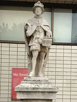 A stone statue of Edward VI. Edward wears a crown and holds a parchment in his left hand and a sceptre in his right hand. The king stands on a stone plinth.