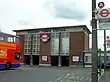 A red-bricked building with a rectangular, grey sign reading "SUDBURY TOWN STATION" in black letters all under a blue sky