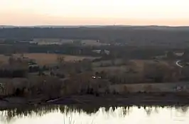 Looking across the Arkansas River from an overlook on Reed Mountain, the flat farmlands of the Arkansas River Valley stands in stark contrast to the mountain itself. Trees, roads, and homes are scattered along the river bottoms, and elevation slowly rises in the distance. Far in the background are the outlines of mountains in the orange-red sunset-colored sky