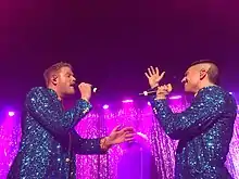 Scott Hoying and /mitch Grassi wearing sparkly suits, facing each other singing onstage.