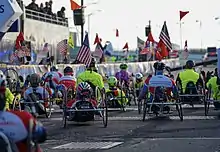 Multiple competitors in a mixture of high and low stance handcycles, all facing away from the camera.