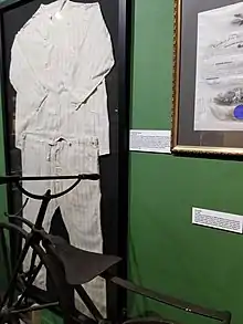 A pair of oversized pajamas on display in a wall case, surrounded by other museum artifacts.