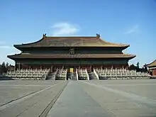 Color photo taken frontally on a sunny day of a stately Chinese-style building with a double roof. The plaque on the building says "Taimiao" ("imperial ancestral temple") in Chinese and in Manchu. The temple is placed on an elevated platform and surrounded by three layers of white fences placed at different heights. Three different flights of stairs lead to the building.