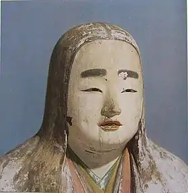 Head and shoulder portrait of a female statue with long hair, painted eyebrows, colored lips and cloths.