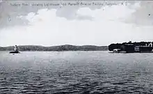 A black-and-white illustration showing the lighthouse at left surrounded by water and the shore at right. Faint writing across the top reads "Hudson River, showing Lighthouse and Maxwell–Briscoe factory, Tarrytown, N.Y."