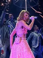 A young white woman singing on a microphone, wearing a polka-dot pink two piece dress