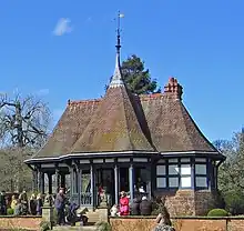 People sitting on a wall in front of a single-storey black-and-white building with steep roofs and a spire