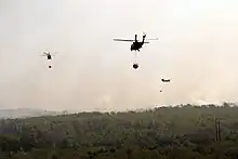 Photograph of three helicopters carrying buckets of water over a burning forest