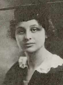 A young white woman wearing a mortar board and academic robe, with a white ruffle-trimmed collar