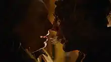 An infected human moves in to kiss a shocked woman, with tendrils connecting their mouths.