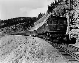 Boxcab electric locomotive pulling a passenger train in a canyon