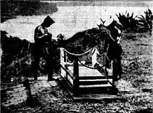 a black and white photograph of two New Guinea sailors with arms reversed standing alongside a grave overlooking the water