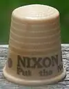 An off-white thimble, with the visible black lettering, "NIXON/Put the ne ...