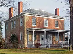 A brick house with a peaked roof pierced by three tall brick chimneys and a white wooden front porch