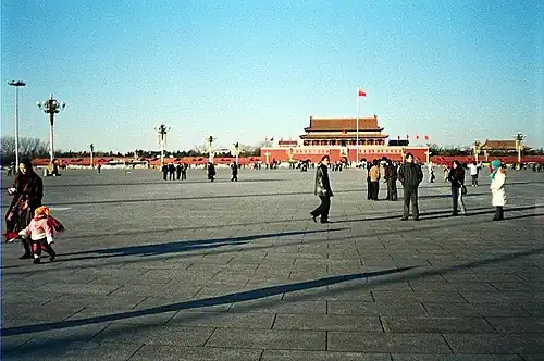 Groups of people wander around Tiananmen Square in the late afternoon. The eponymous Tiananmen, literally "Gate of Heavenly Peace", sits in the background.