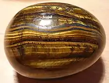 "Photograph of a polished ovoid stone with bands containing shimmering golden fibers"