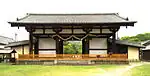 Low and wide wooden gate with white walls and a gabled roof.