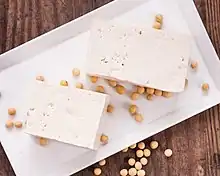 This is a picture of tofu on a plate surrounded by soybeans.