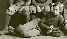 Posed sepia-toned photograph (apparently cropped from a team photograph) of Hughitt wearing a football uniform reclining on the floor