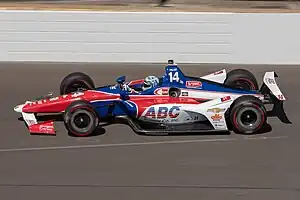 A red, white and blue racing car being driven at high speed on an oval race track