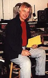 A grey-haired man with glasses and a black shirt standing in front of a microphone