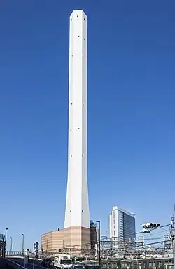 Ground-level view of a tall, white, angular chimney rising from a brown, striped building