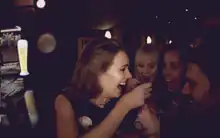 Three women and a man laughing and making a toast in a club.