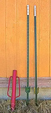 Two T-posts and red post pounder (or driver) used to drive them into the ground.  The flat plate helps stabilize the post, which is driven into the ground until the plate is buried.