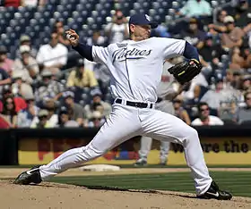 A man in a white baseball uniform in his pitching motion.