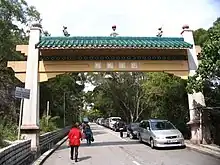  Cars parked on one-side of a tree-lined street with pedestrians walking under an archway which crosses the street