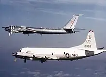 Two aircraft in-flight. One a twin-prop aircraft in the foreground, another is a larger four-prop aircraft with swept-back wings.