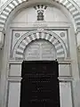 A mausoleum door, topped by a commemorative inscription.