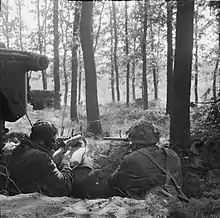 Two men facing away from the camera armed with Sten guns