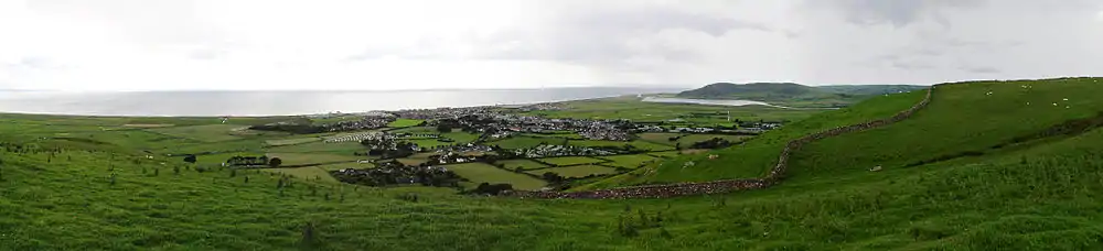 Panorama of the Welsh town Tywyn showing it nestled between hills and with the sea behind. A reservoir is visible in the background.