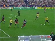 A coloured action photograph of a football match in progress. There are a group of men, four of which wearing yellow shirts and black shorts. Five are wearing red and blue striped shirts.