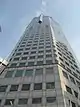 Ground-level view of a 40-storey skyscraper with an octagonal cross section and a protruding, triangular ledge near the 20th floor