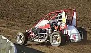 A midget car being driven on a dirt race track.