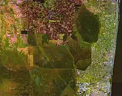 A color satellite image of the northern Everglades showing green chunks of Everglades surrounded by white settlement areas of the South Florida Metropolitan Area to the east and red agricultural fields in the Everglades Agricultural Area to the north