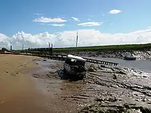 Muddy river bank with a small boat on it. Water can still be seen in the channel to the right.