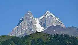 A double-peaked, snow-covered mountain under cloudless blue sky