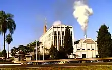 Photo of shorter building with smoke coming out of smokestack next to five-story office building