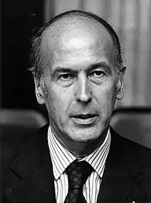 A candid head shot of Valéry Giscard d'Estaing who is looking neutral, wearing a dark jacket, dark tie and a white formal shirt with darker vertical stripes.