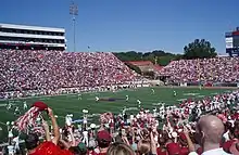 American football players line up for a kickoff on an American football field surrounded by crowded stands.