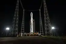 A rocket sits at a launch pad at night, illuminated by floodlights