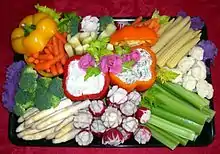 Brightly colored veggie platter arranged over purple cabbage with "rosebud radishes" and sweet peppers used as serving containers