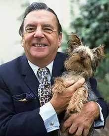 A smiling middle-aged man holds a small dog.