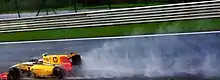 A black, yellow and red Formula One car racing at speed on a wet track