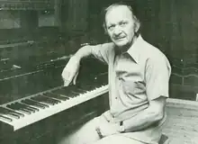 A Caucasian man rests his arm on a piano